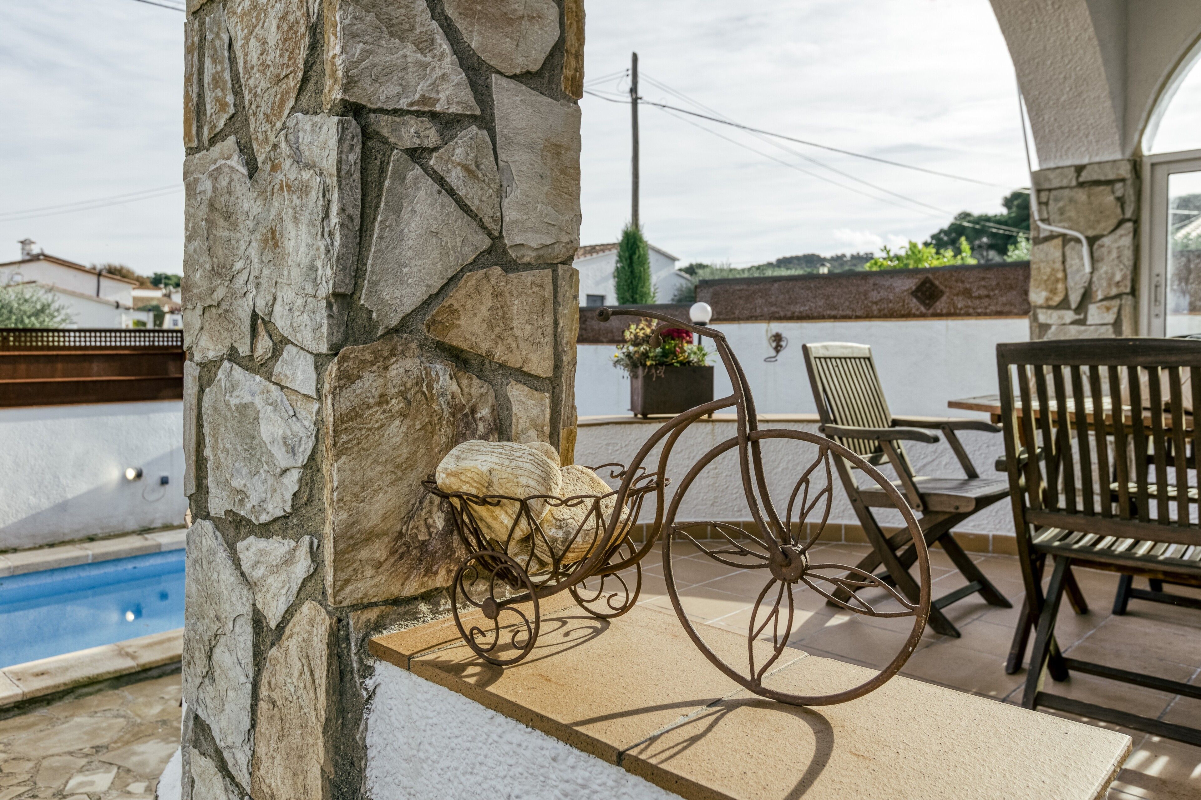 A stone pillar, a metal chair, a wooden bench, and a small table with a flower pot.
