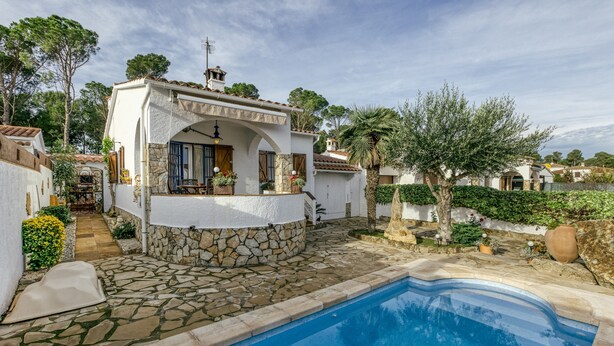 A poolside villa with a stone pool, white exterior, and a small bar area.