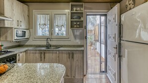 A kitchen with a granite countertop, wooden cabinets, a microwave, a sink, and a refrigerator.