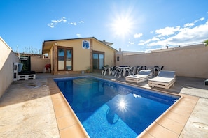 A swimming pool with lounge chairs, a small building with a sign, and a clear sky. - Holiday Home "Faro" with Pool, Garden & Wi-Fi (Camarles)