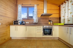 A kitchen with wooden walls, a window with curtains, a microwave, an oven, and a sink. - Holiday Home "Faro" with Pool, Garden & Wi-Fi (Camarles)
