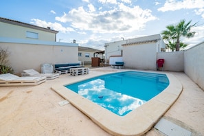 Una piscina con sillas de descanso y una palmera en un barrio residencial.