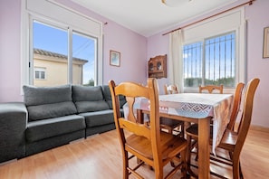 Una habitación con sofá, mesa de comedor, sillas, un armario y ventanas amplias.