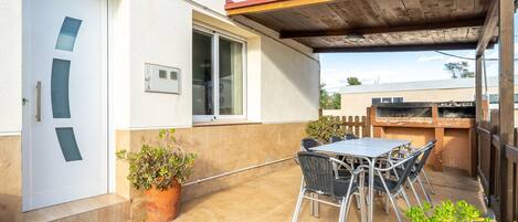 A patio with a table and chairs, a potted plant, and a barbecue grill.