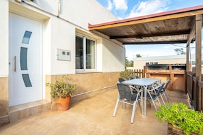 Un patio con una mesa, sillas, una planta en maceta y una parrilla.