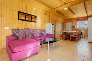 Ein Holzinterieur mit einer Couch, einem Esstisch, Stühlen, einem Kühlschrank und einer Waschmaschine.