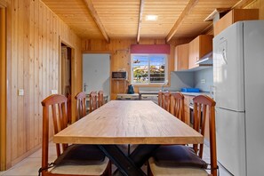 Ein Zimmer mit Holzwänden, einem Esstisch, Stühlen, einem Kühlschrank und einem Fenster mit Blick.