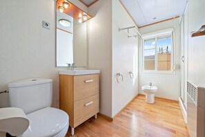 Une salle de bain comprenant des toilettes, un lavabo, un meuble-lavabo, un miroir et une fenêtre.