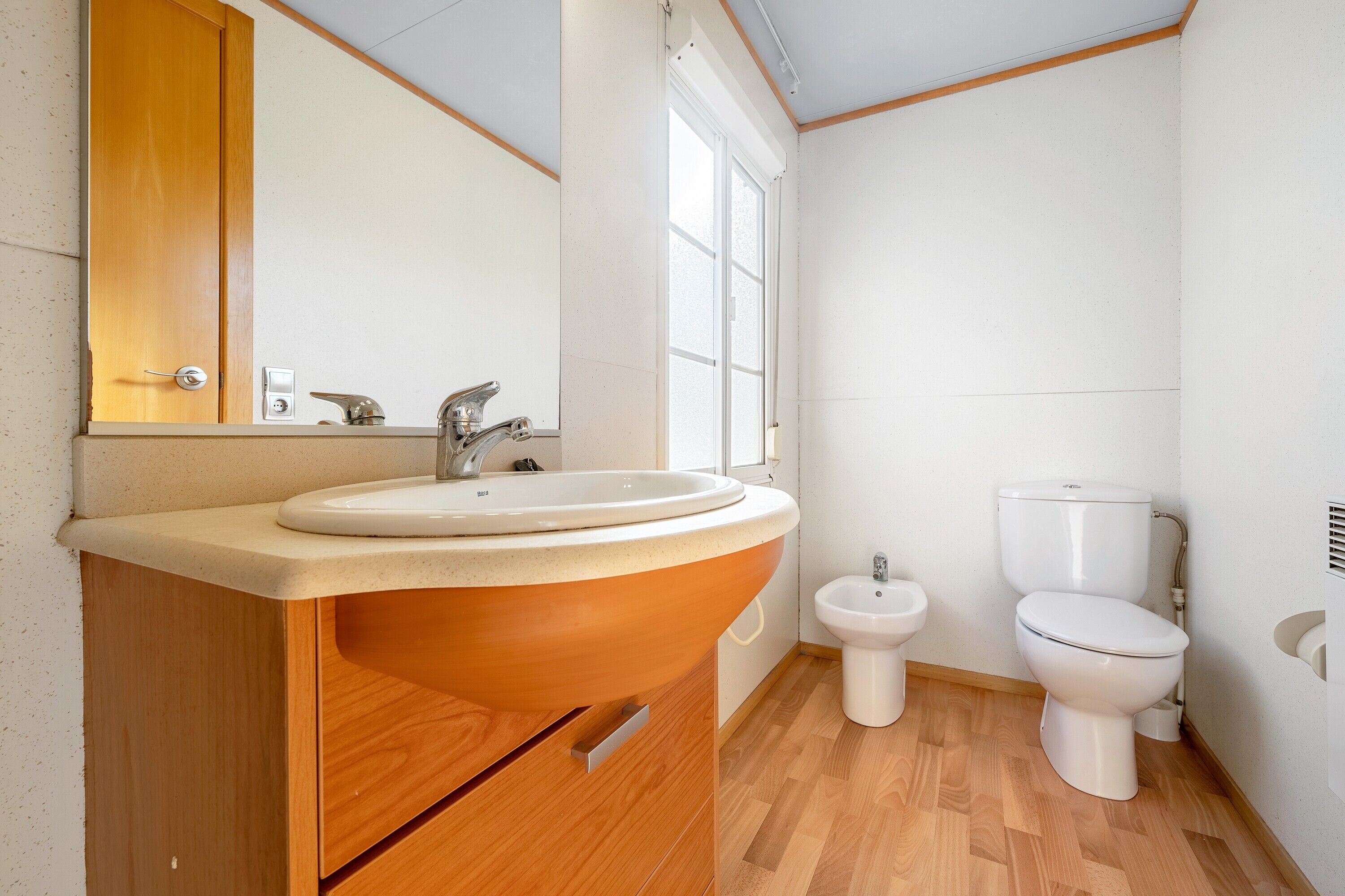 Une salle de bain avec un meuble-lavabo en bois, un évier, un miroir, des toilettes et un bidet.
