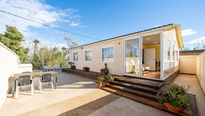 A single-story house with a patio, a dining area with chairs, and a door leading to a room. - Holiday Home "La Marquesa" with Shared Pool, Garden & Wi-Fi (Camarles)