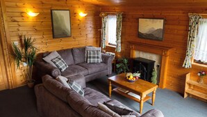 A cozy living room with a sectional sofa, a fireplace, and wooden walls. - Whiteside Lodge at Burnside Park (Keswick)