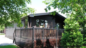 A wooden cabin with a deck, surrounded by trees and a grassy area. - Whiteside Lodge at Burnside Park (Keswick)