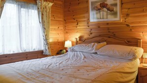 A wooden cabin bedroom with a bed, a nightstand, a lamp, and a framed picture on the wall. - Whiteside Lodge at Burnside Park (Keswick)
