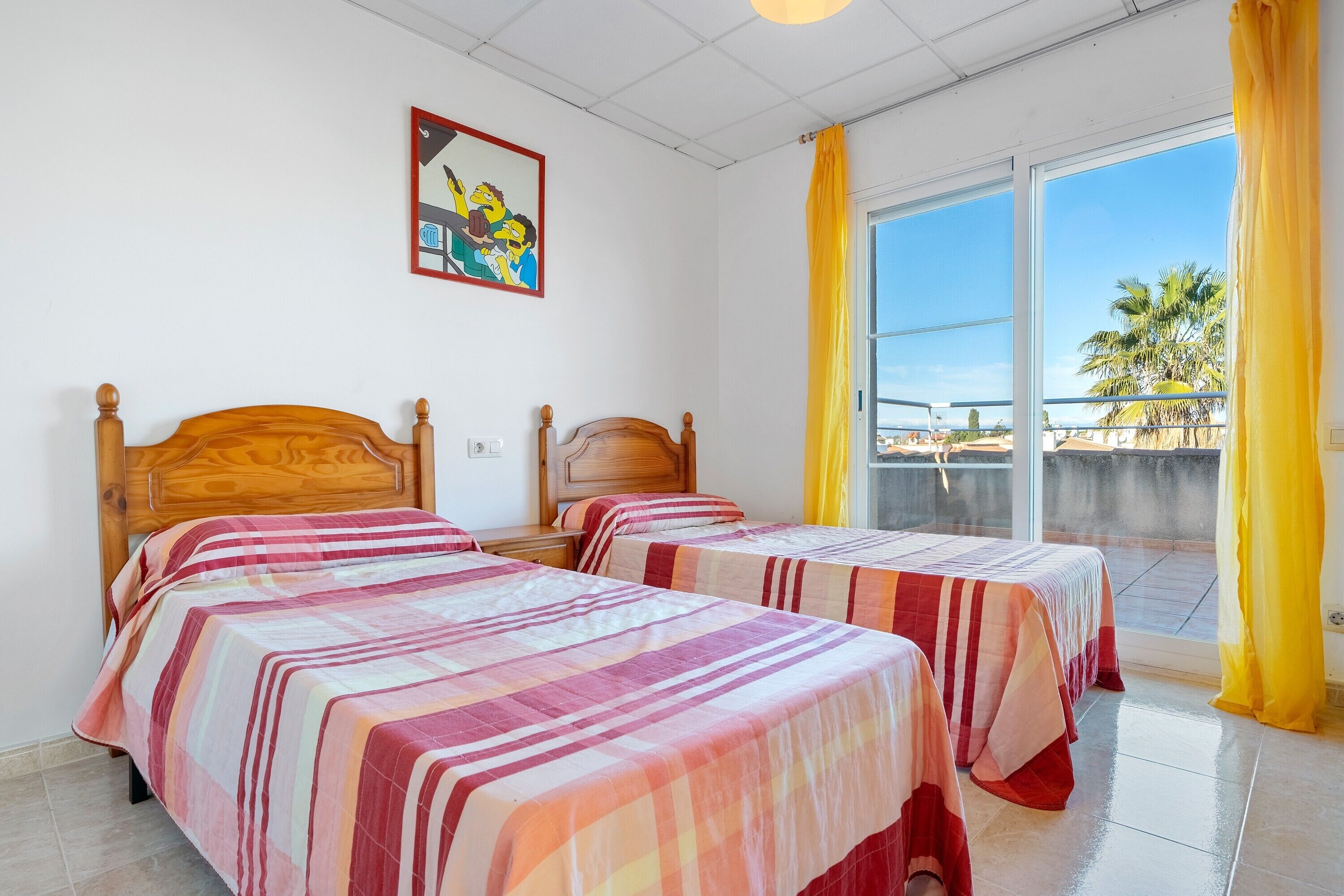 A room with two beds, a painting on the wall, and a view of palm trees through the window.