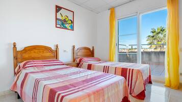 A room with two beds, a painting on the wall, and a view of palm trees through the window.