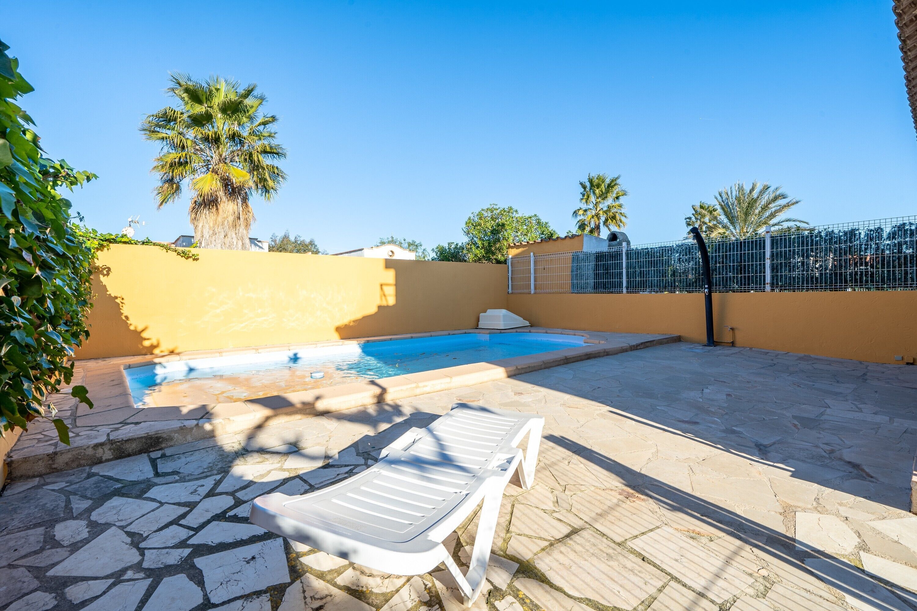 A swimming pool with a white lounge chair, a stone patio, and a yellow wall.