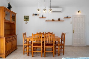 A dining area with a wooden table and chairs, a wooden cabinet, wall-mounted lights, and a white door. - Holiday Home "Chalet l'alba" with Pool, Garden & Wi-Fi (deltebre)