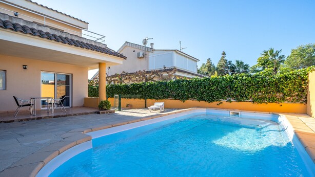 Une piscine avec un espace patio ensoleillé, un coin salon abrité et une haie.