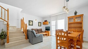 Un salon comprenant un canapé, une table à manger, des chaises, un escalier en bois et un téléviseur.