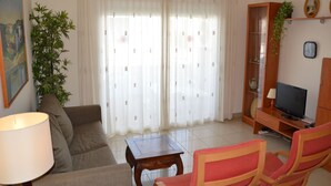 Un salon comprenant un canapé, des fauteuils, une table basse, un téléviseur, une lampe, une plante et une bibliothèque.