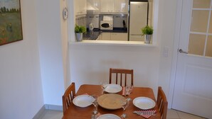 Une table à manger dressée avec des assiettes, des verres et des couverts, une chaise en bois et une petite plante en pot posée sur le comptoir de la cuisine.