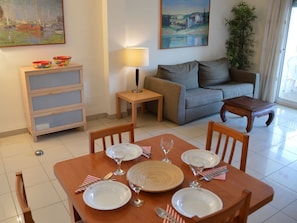 A dining area with a wooden table set for four, a sofa, a lamp, and a plant.
