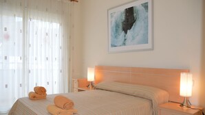Une chambre d’hôtel avec un lit, deux tables de chevet, une commode, une fenêtre avec des rideaux et un tableau au mur.