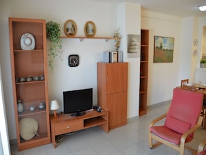 A living room with a TV, wooden furniture, a clock, and a dining area with a chair.