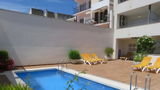 Une piscine avec des chaises longues, un petit jardin et un bâtiment doté de balcons.