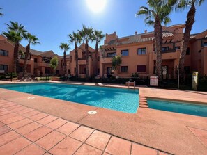 Une piscine dont le fond est recouvert de carrelage, entourée de palmiers et bordée d’un immeuble doté de nombreux balcons.