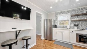 A modern kitchen with a flat-screen TV, stainless steel appliances, white cabinets, and a patterned backsplash. - Private 1BR Cottage In Downtown Historic Norcross (Norcross)