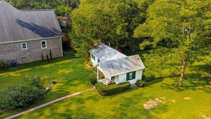 A two-story house with a brick exterior and a white front door, surrounded by a well-maintained lawn and trees. - Private 1BR Cottage In Downtown Historic Norcross (Norcross)