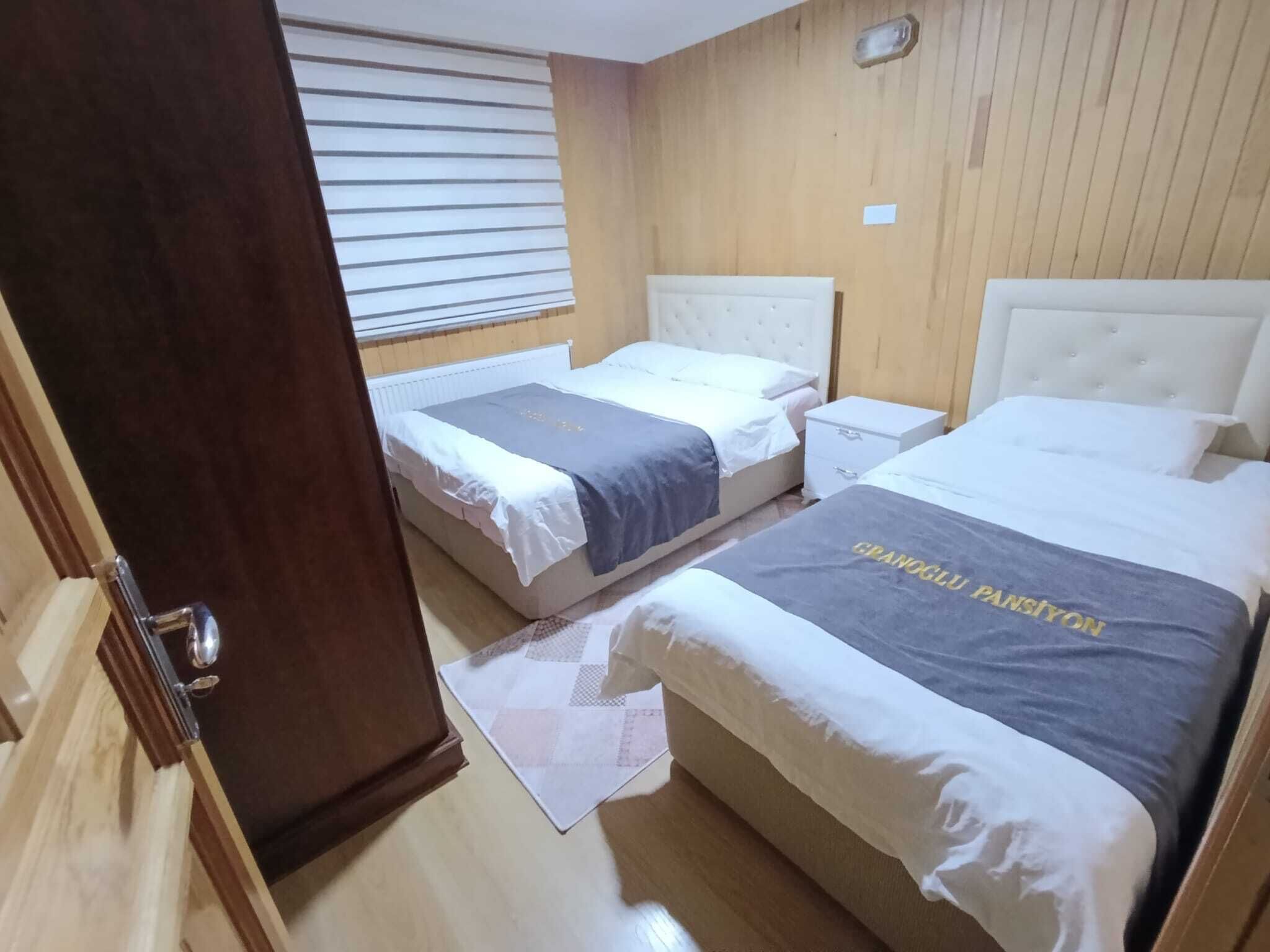 Una habitación con dos camas, una pared de madera, una ventana con persianas y una puerta.