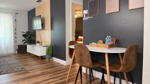 Moderni ruokailutila, jossa on pyöreä pöytä, kaksi ruskeaa tuolia, valkoinen sivupöytä ja harmaa tehosteseinä.