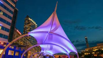 A nighttime view of the Tampa Riverwalk with a sail-like structure in the foreground and buildings in the background.