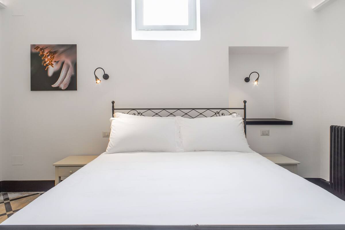 A neatly arranged bedroom with a bed, bedside tables, and a small window.