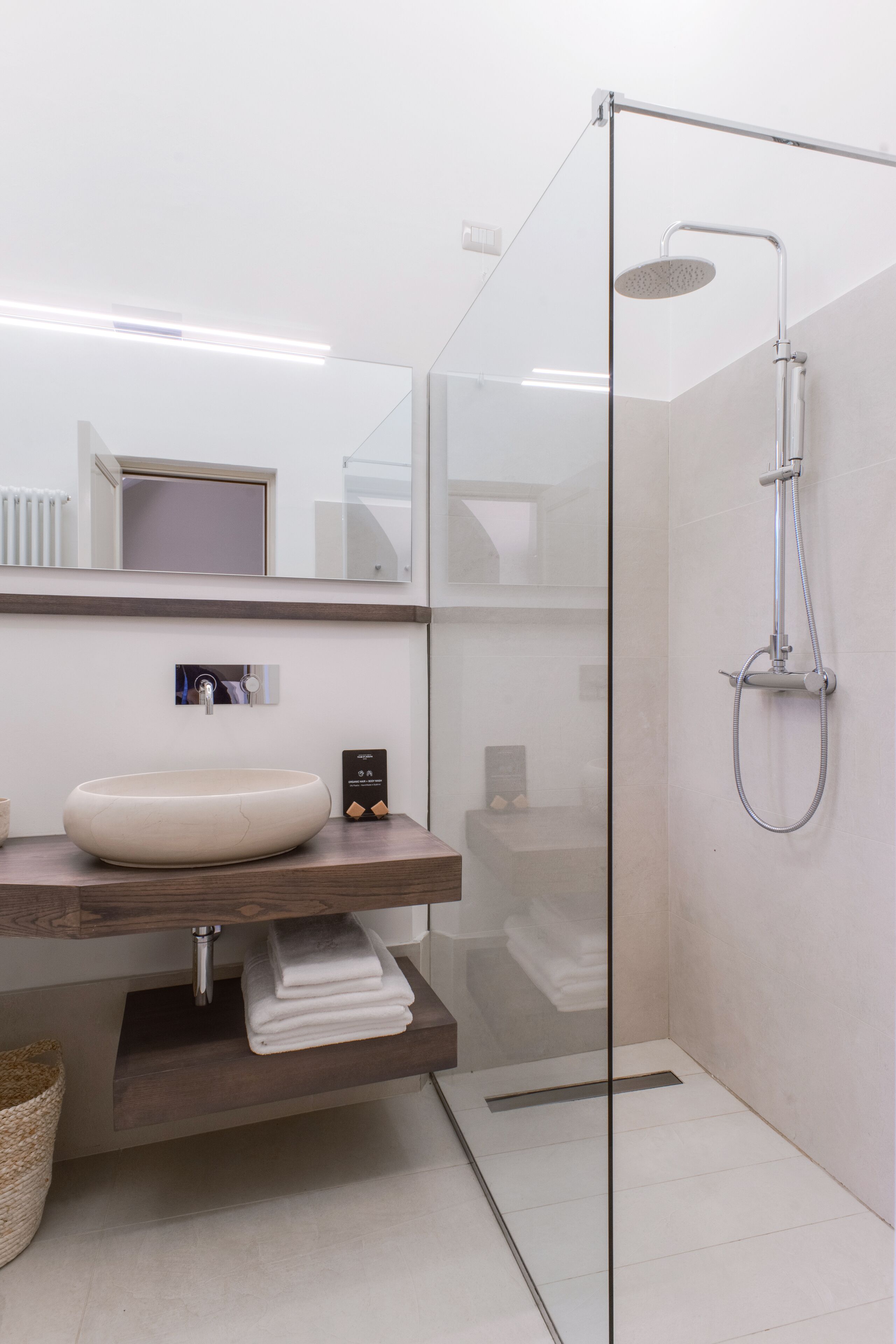 A modern bathroom with a glass-enclosed shower, a wooden vanity, and a large mirror.