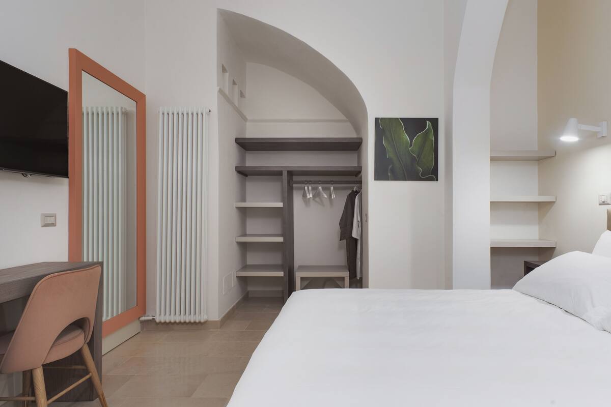 A modern bedroom with a bed, a desk, a chair, a wardrobe, and a TV.