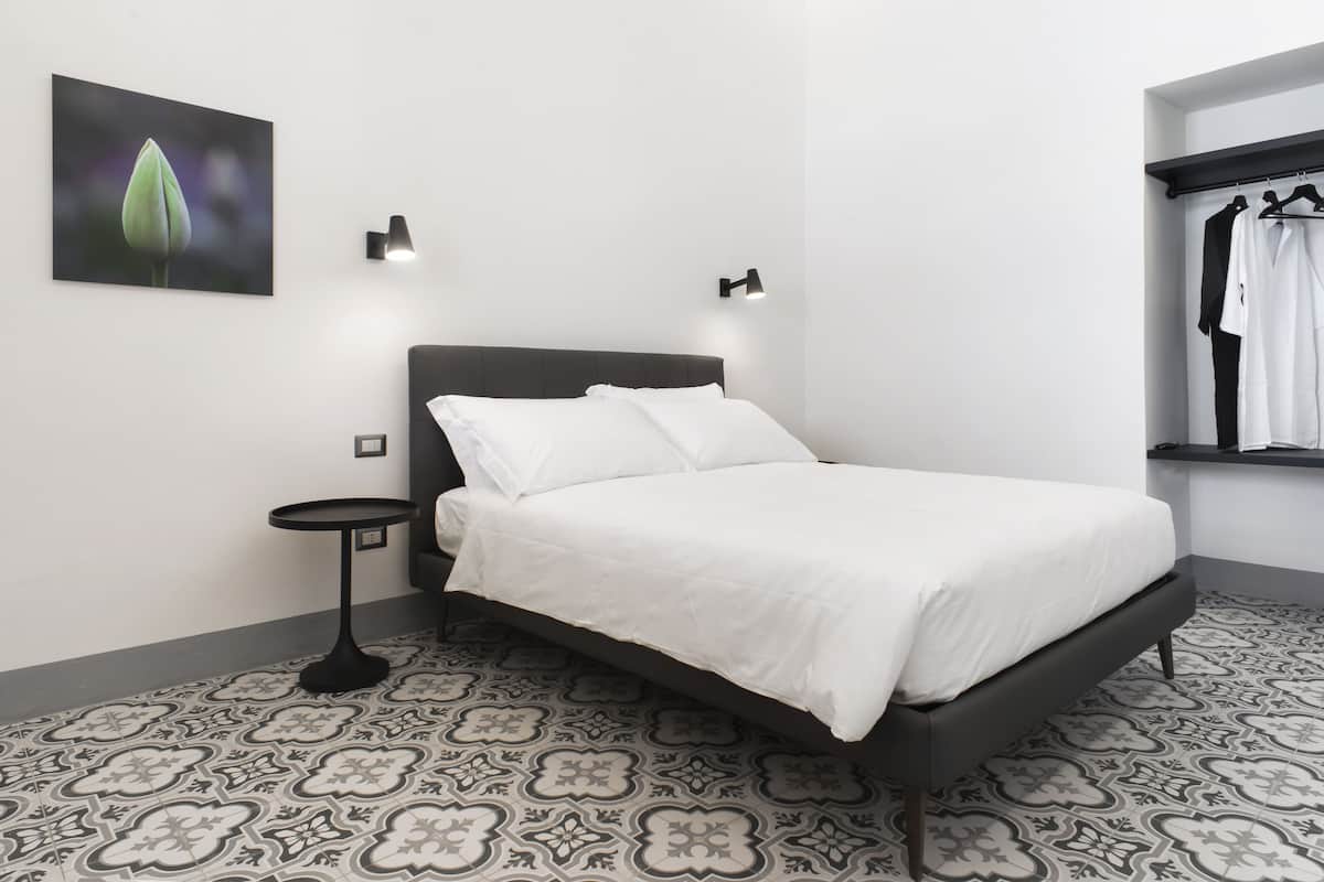 A modern bedroom with a large bed, two bedside tables, and a wall-mounted light fixture.