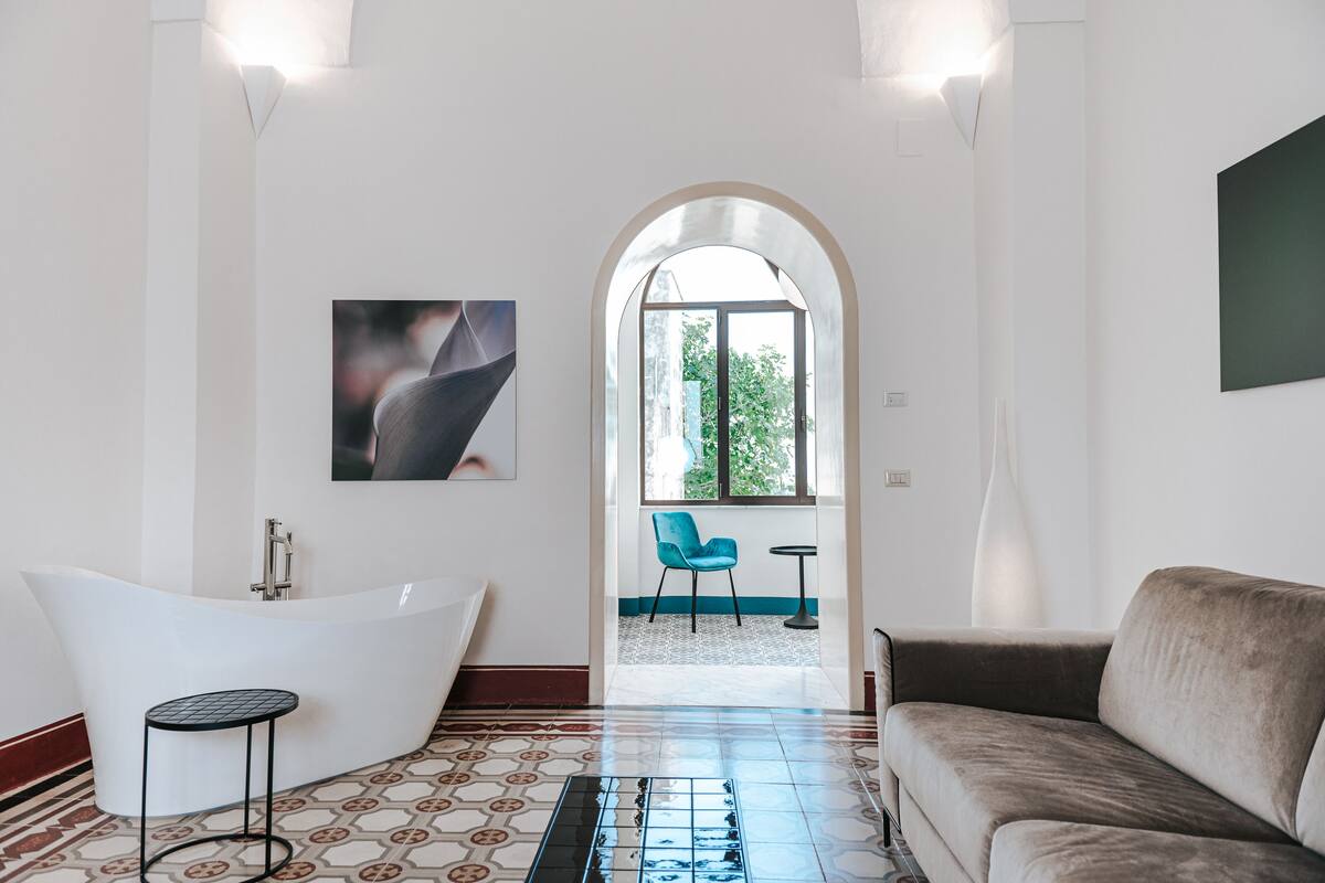 A modern bathroom with a freestanding bathtub, a small round table, and a blue chair.
