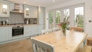 Eine moderne Küche mit weißen Schränken, einer Holz Arbeitsplatte und einem eingebauten Backofen. Es gibt einen Esstisch mit Stühlen und eine Blumenvase.
