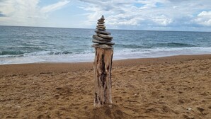 Ein hölzerner Pfosten mit einer Steinhaufen am Strand, im Hintergrund das Meer.