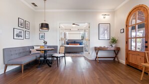 Un salón espacioso con suelo de madera, un sofá gris, una mesa redonda con sillas y un escritorio de madera.