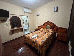 A bedroom with a wooden bed, a built-in TV, a wardrobe, and a bathroom visible through a glass door. - OYO Hotel Puerto Real Minatitlán (Minatitlán)