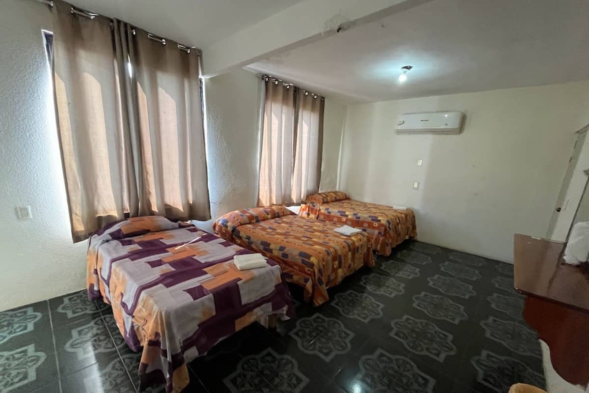 A room with two beds, a tiled floor, an air conditioning unit, and a window with curtains.