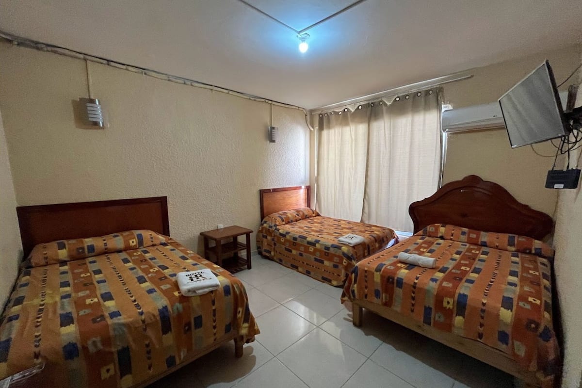 A hotel room with three beds, each with patterned bedding and a small bedside table.