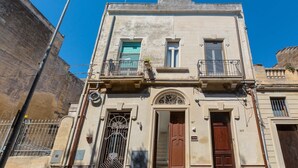 A two-story building with a central entrance, a balcony on the upper floor, and a metal gate on the ground floor. - 2018 Mimì Maison by Barbarhouse (Lecce)