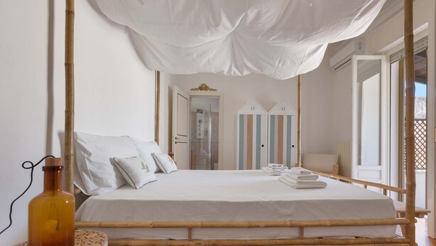 A bed with a canopy, a bedside table with a bottle, and striped doors in the background. - 2018 Mimì Maison by Barbarhouse (Lecce)
