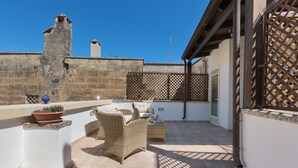 A rooftop patio with wicker furniture, a potted plant, and a view of a historic stone wall. - 2018 Mimì Maison by Barbarhouse (Lecce)