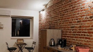 A compact kitchen with a brick wall, wooden cabinets, and a dining area with two chairs.